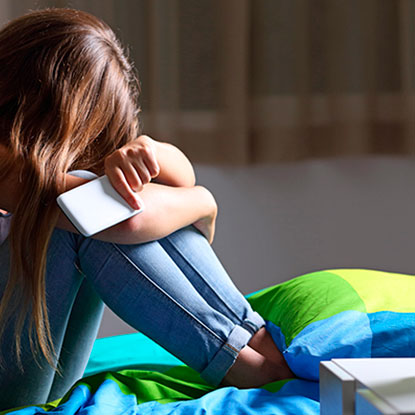 Joven triste ocultando su rostro con un smartphone, ilustrando la importancia de las reglas de convivencia digital para proteger la autoestima.