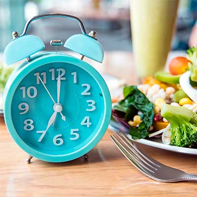 Ayuno intermitente un reloj que indica las horas para comer con una ensalada al lado
