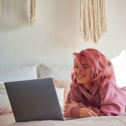 Joven con cabello teñido de rosa sonriendo frente a su laptop, representando el desarrollo del amor propio en adolescentes en la era digital.