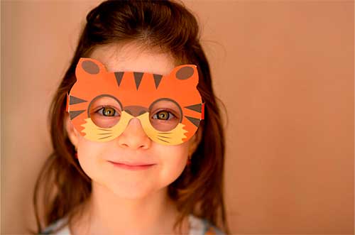 Niña pequeña usando una máscara de tigre hecha a mano, una idea de **disfraces con material reciclado fáciles** utilizando cartón y cartulinas de colores.