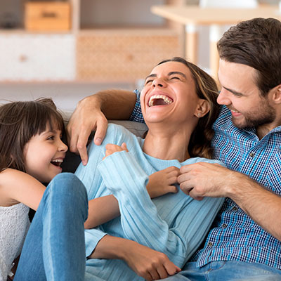 Familia sonriendo y riendo junta en el sofá de su casa, reflejando felicidad, salud emocional y bienestar mental.