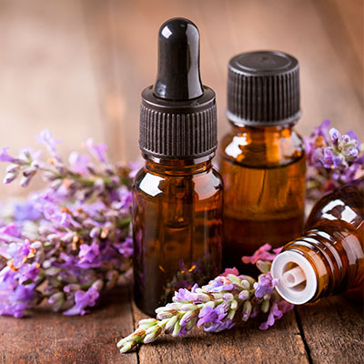 Frascos de aceites esenciales para problemas respiratorios sobre una mesa de madera con flores aromáticas.