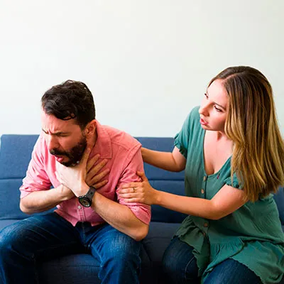 Hombre con signo universal de asfixia recibiendo primeros auxilios por obstrucción de vías respiratorias.