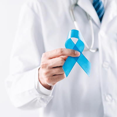 Médico con bata blanca sosteniendo un lazo azul como símbolo de las medidas para prevenir el cáncer de próstata y promover la salud masculina.