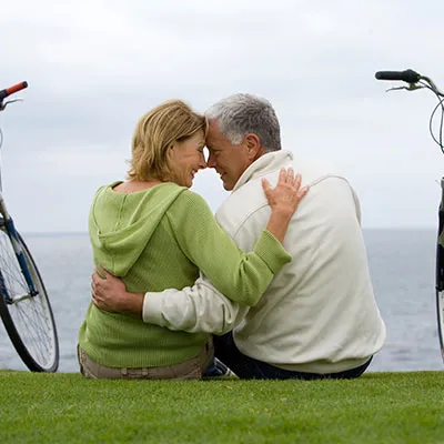Una pareja de adultos mayores demostrando su amor en pareja abrazados frente al mar con sus bicicletas a los lados.