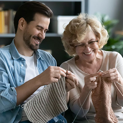 Hombre y su madre de más de 60 años tejiendo juntos y riendo mientras hacen manualidades