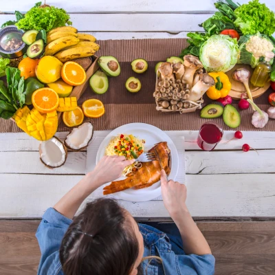 Mujer sentada a una mesa con variedad de frutas, verduras y pescado, analizando su dieta para identificar alimentos que inflaman la tiroides y mejorar su metabolismo.