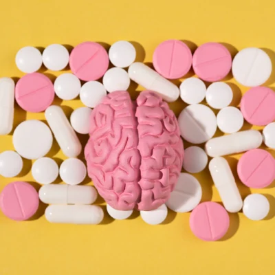 Modelo de cerebro humano rodeado de píldoras y cápsulas médicas sobre un fondo amarillo, que representa la regulación de la serotonina en adultos mayores y la salud neurológica.