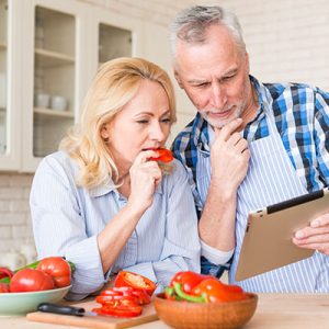 pareja mirando tableta digital mientras prepara la comida
