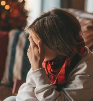 Persona atravesando el duelo en Navidad, sentada en un sofá con decoración navideña al fondo, expresando tristeza y recogimiento emocional.