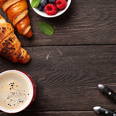 Mesa de madera con café espumoso, croissants recién horneados y bowl de frutos rojos para un brunch en casa saludable.