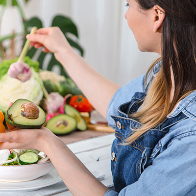 Mujer preparando una ensalada con aguacate y vegetales frescos como parte de una dieta antiinflamatoria.