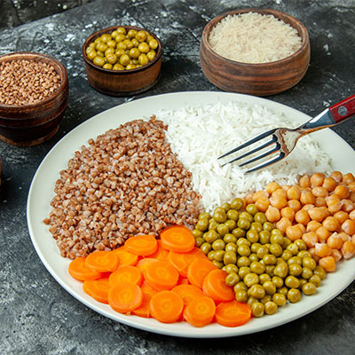 Cereales integrales y legumbres para reducir la inflamación. Plato con quinua, arroz integral, garbanzos, arvejas y zanahorias, representando fuentes de proteína vegetal en una dieta antiinflamatoria.