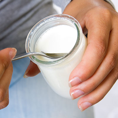 Mujer sosteniendo un frasco de yogur natural, uno de los alimentos ricos en calcio para fortalecer los huesos según expertos de Colmédica.