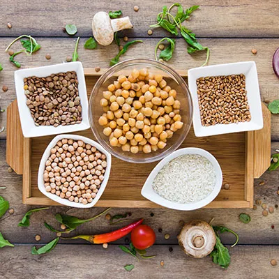 Variedad de carbohidratos complejos como garbanzos, lentejas, arroz y granos integrales en cuencos de cerámica sobre una mesa de madera.