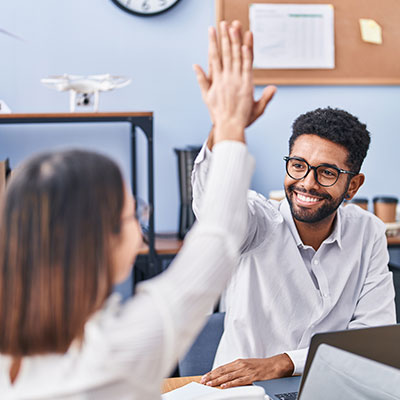 Un hombre y una mujer celebrando un logro laboral con un choque de palmas, representando la superación del síndrome del impostor y la autovaloración profesional.