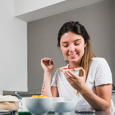 Mujer joven sonriendo mientras disfruta de un desayuno equilibrado con pan integral y frutas, siguiendo las claves para incluir carbohidratos complejos en su alimentación.