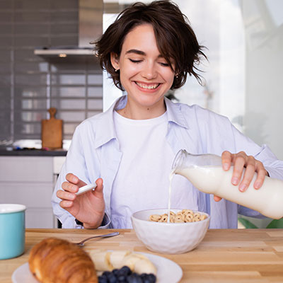Mujer sonriente sirviendo leche en un tazón de cereal, ilustrando los mitos sobre si los lácteos son la única fuente de calcio para los huesos.
