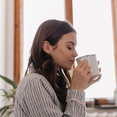 Mujer disfrutando de una taza de café de forma pausada, representando las claves para un consumo de cafeína que no afecte la salud.