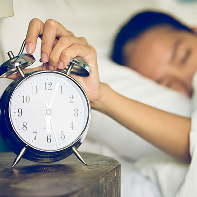 Persona apagando un reloj despertador por la mañana para regular su ciclo circadiano y sueño.