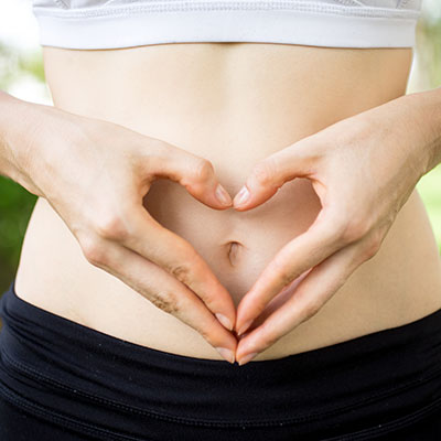 Persona haciendo un corazón con las manos sobre su vientre, representando la salud digestiva y el equilibrio de la microbiota intestinal.