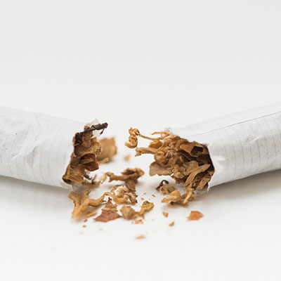 Cigarrillo roto por la mitad mostrando el tabaco interior sobre un fondo blanco, simbolizando la decisión de dejar de fumar y los beneficios para la salud.