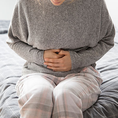 Mujer sentada con dolor abdominal tipo cólico causado por una infección por la bacteria Escherichia coli.