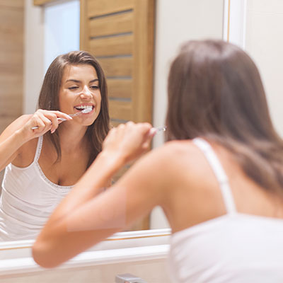 Mujer cepillándose los dientes frente al espejo para cuidar su salud oral y rendimiento físico.