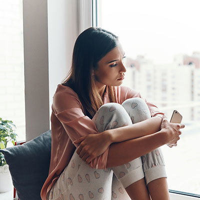 mujer joven pensativa usando un teléfono representando las adicciones digitales