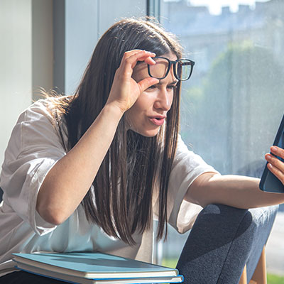 Mujer con gafas levantadas alejando e intentando enfocar la pantalla de su celular debido a síntomas de presbicia o vista cansada.