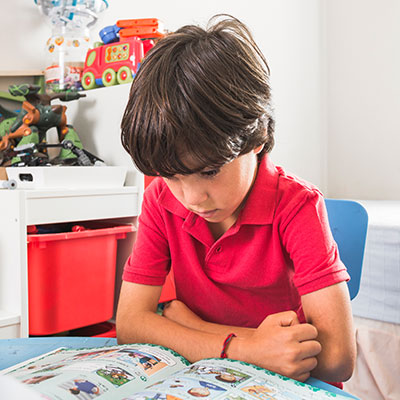 Niño concentrado leyendo un libro en su escritorio preparando rutinas ante la ansiedad infantil por el regreso a clases.