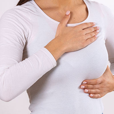 Mujer sosteniendo su seno con dolor manifestando síntomas de mastitis durante la lactancia.