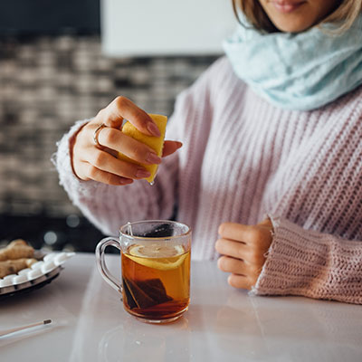 Mujer con bufanda exprimiendo medio limón en una taza de té caliente para aliviar la tos con flema.