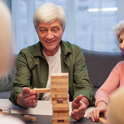 Adultos mayores de más de 60 años compartiendo y jugando un juego de mesa de bloques de madera en un espacio de integración social.