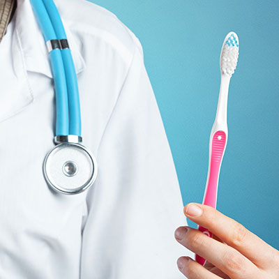 Mano sosteniendo un cepillo de dientes junto a un profesional de la salud con estetoscopio, representando la relación entre hábitos orales y salud cardiovascular.