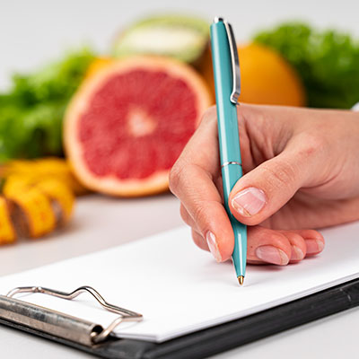 Mano escribiendo recomendaciones y plan de alimentación saludable sobre una libreta para cuidar el hígado graso